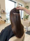 Back view of long straight glossy dark brown hair with tape-in extension wefts visible near the roots under a lifted layer (temporary image)